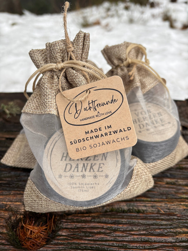 Handgemachte Mini-Duftkerzen in schwarzen Dosen mit getrockneten Blüten und lustigem Aufkleber 'Der hat Gleitzeit' – ideal als Wichtelgeschenk aus Sojawachs.