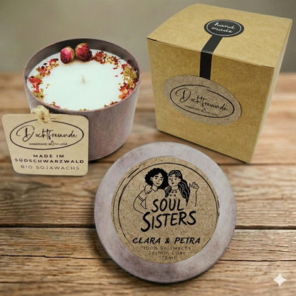 Handgemachte, personalisierte 'Soul Sisters' Sojawachskerze von Dochtfreunde. Das Bild zeigt die offene Kerze mit Blüten- und Rosendekor im braunen Gefäß, den Deckel mit der Aufschrift 'SOUL SISTERS' und den personalisierten Namen 'CLARA & PETRA' sowie die passende Geschenkverpackung aus braunem Karton