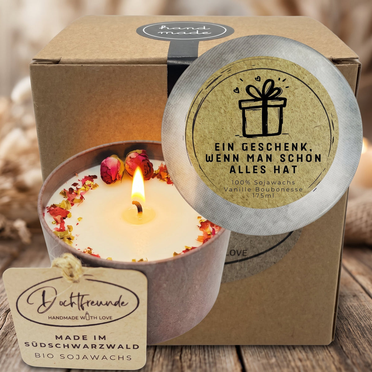 Brennende Vanille-Duftkerze mit Rosenknospen und Blütenblättern in Vintage-Dose vor Geschenkbox mit Deckelspruch